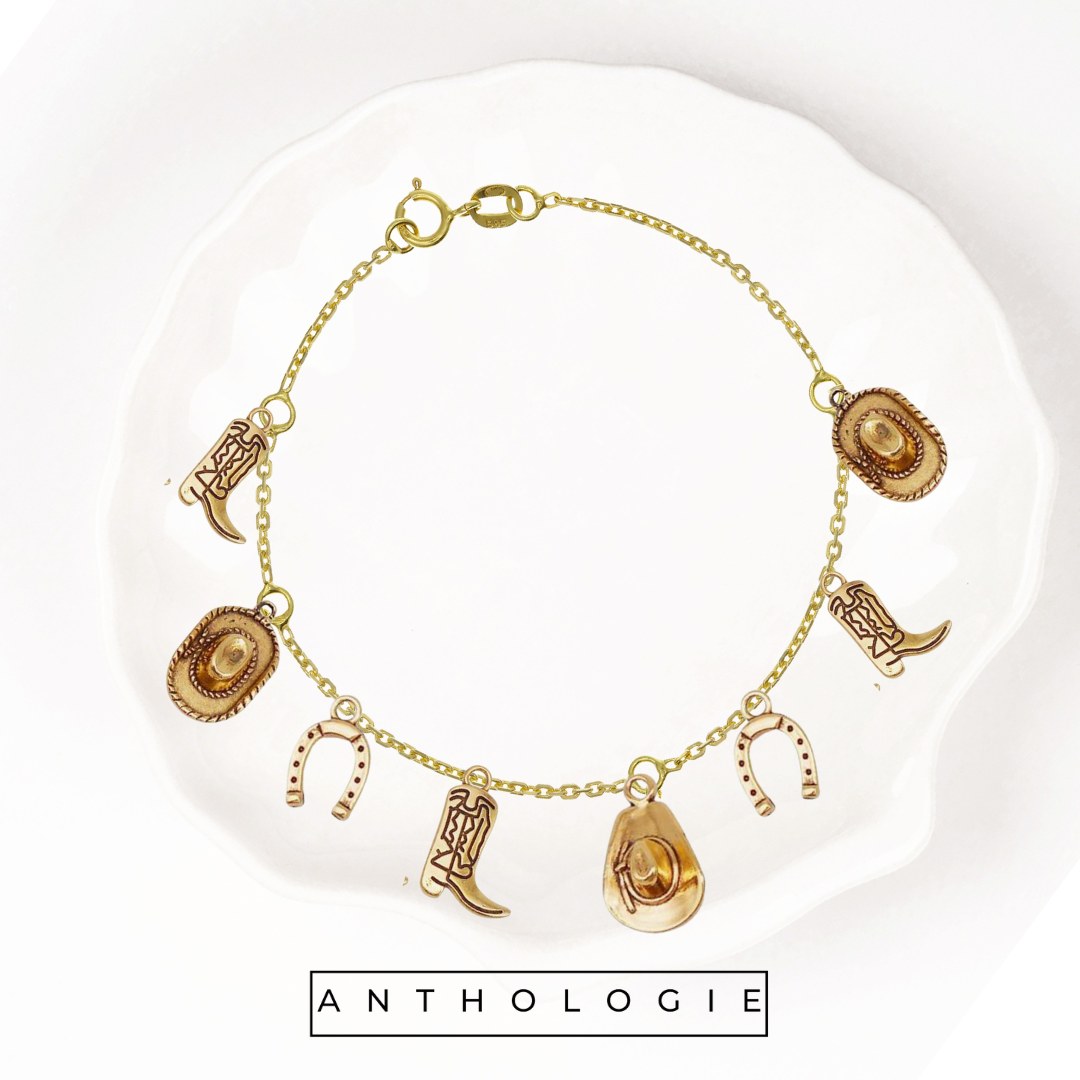 Gold bracelet with charms on a white plate, featuring the brand 'Anthologie'.
