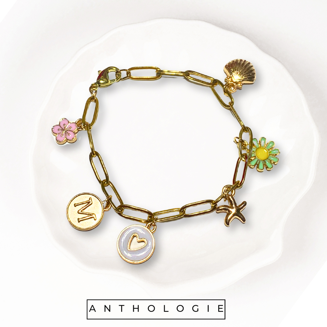 Gold bracelet with various charms on a white plate, featuring the brand 'Anthologie'.