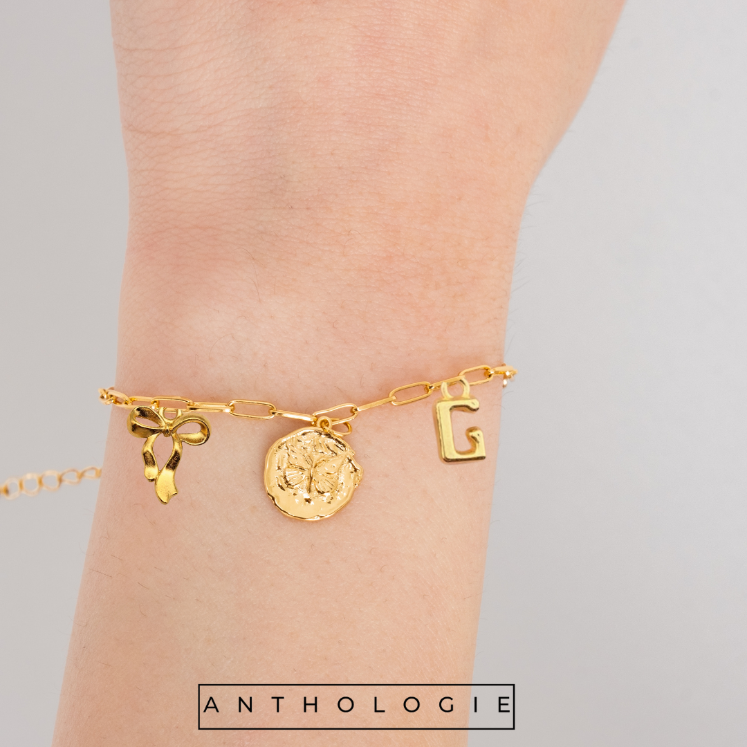 Gold bracelet with charms on a wrist, branded 'Anthologie'.